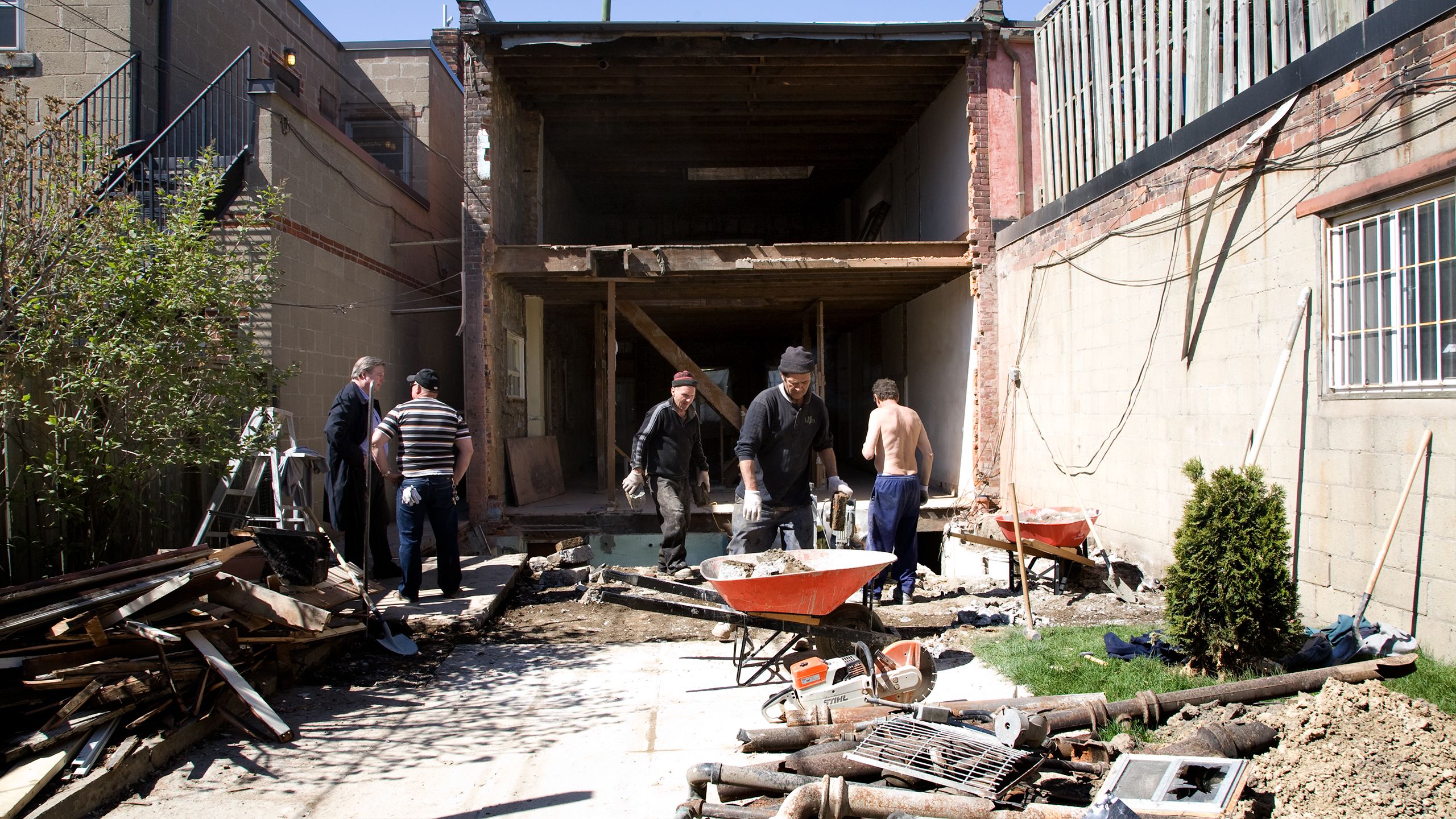 crew clearing debris from the fully removed rear wall of the building.